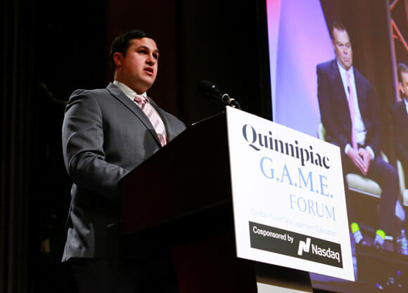 A student stands at a podium on stage at GAME Forum