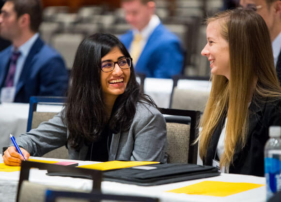 Two students talk while they sit at participant tables during GAME Forum