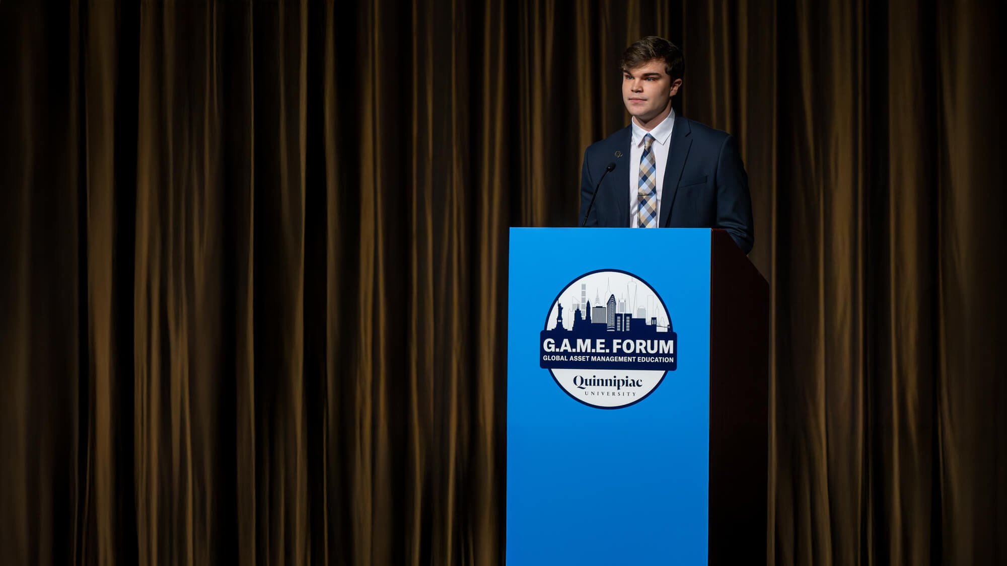 Quinn Guth speaking at a podium during the GAME Forum opening ceremony.