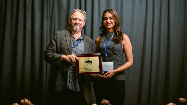 Student and faculty participants in the Graduate Overall category gather on stage with their award at the Forum Awards Ceremony.
