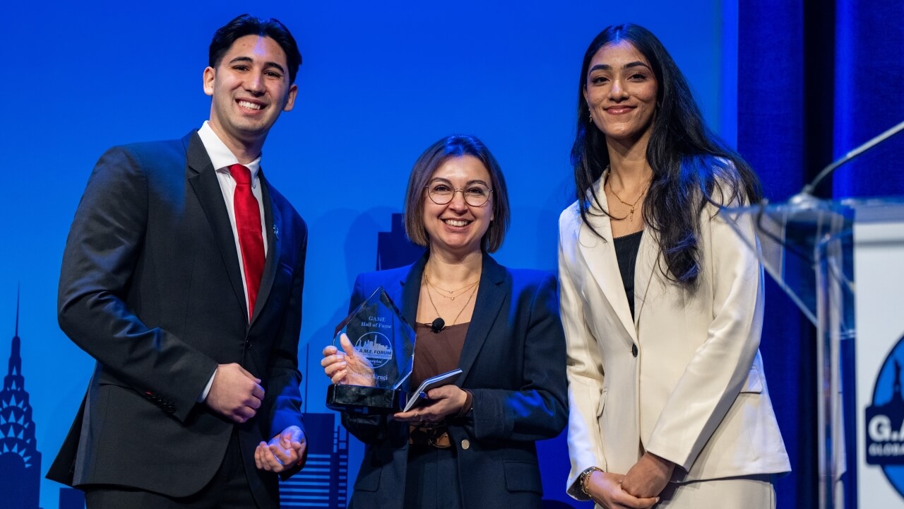 Blerina Uruçi standing between two students holding a glass GAME Hall of Fame award.