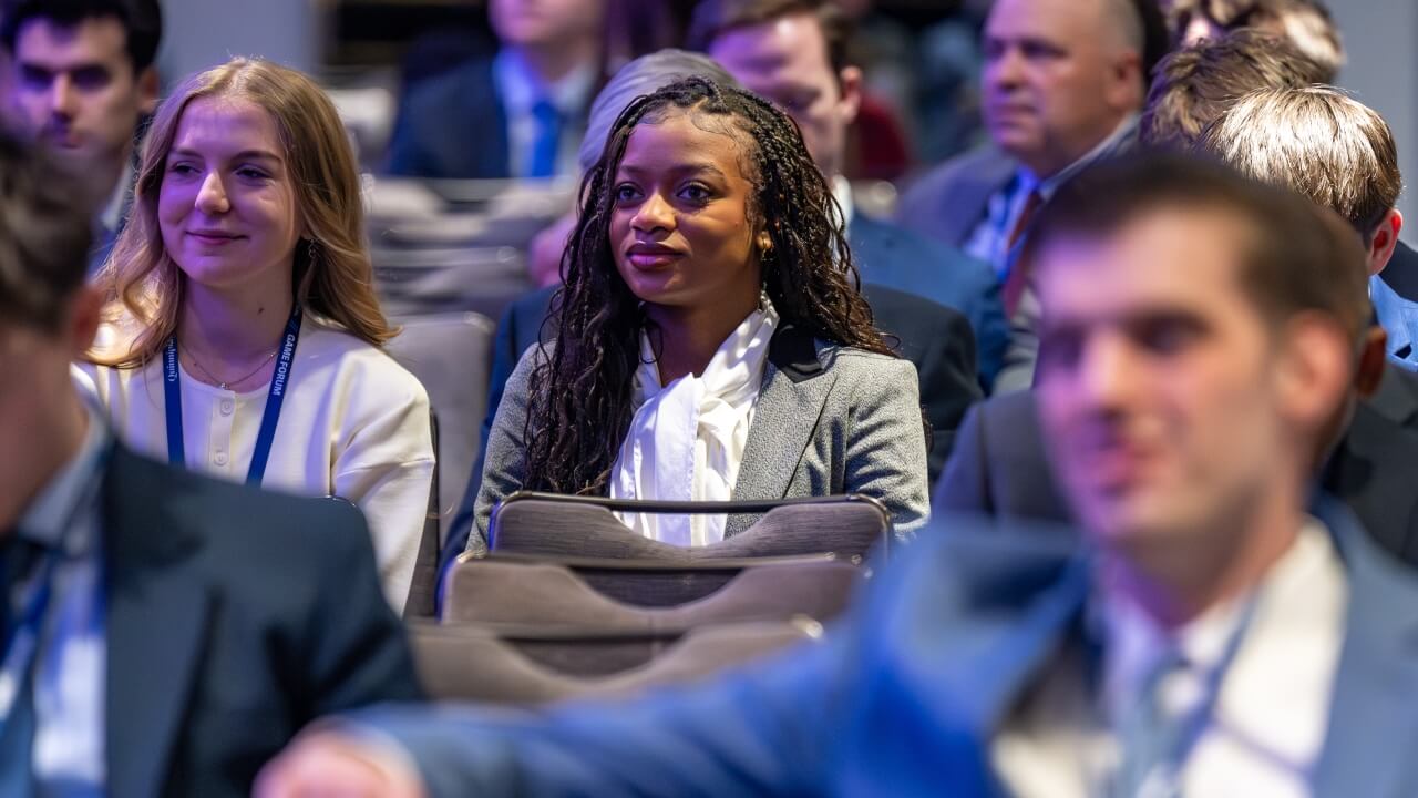 Woman smiles as she sits among fourm attendees.