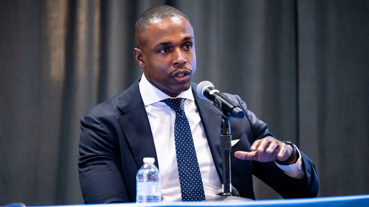 Bilal Little seated at a panel table speaking into a microphone.
