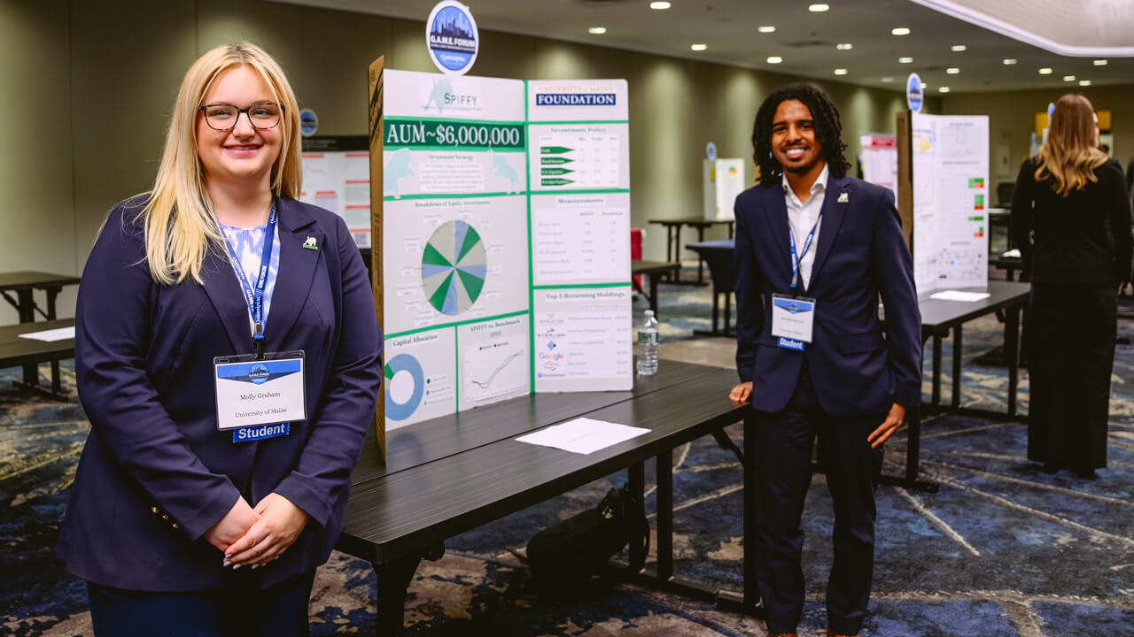 Two University of Maine students display their Assets Under Management poster.