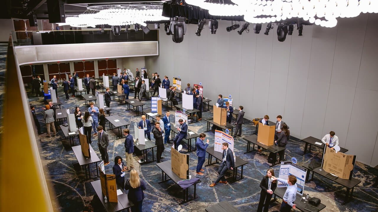 An overhead view of tables of posters on display in a hotel ballroom.