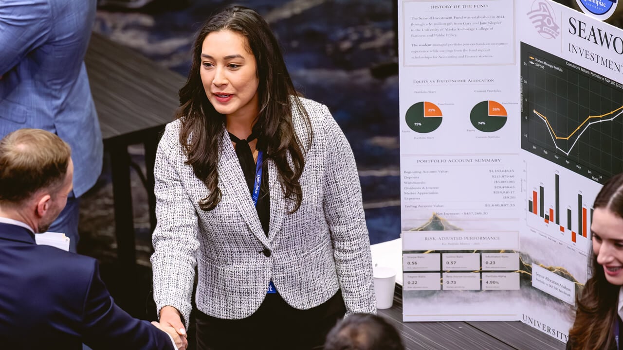 A woman shaking hands with a man in front of her poster presentation.