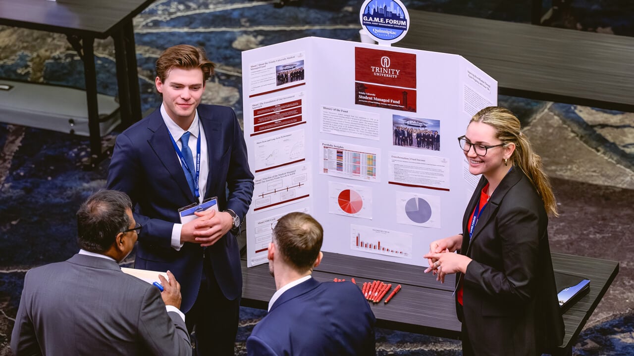 Two Trinity University students standing and smiling in front of their poster.