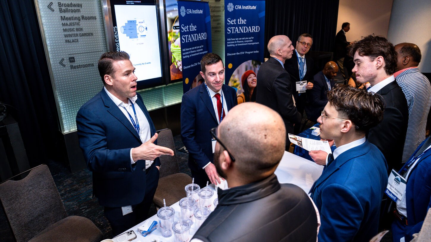 Multiple students engage in a discussion with CFA Institute representatives at a busy exhibit table.