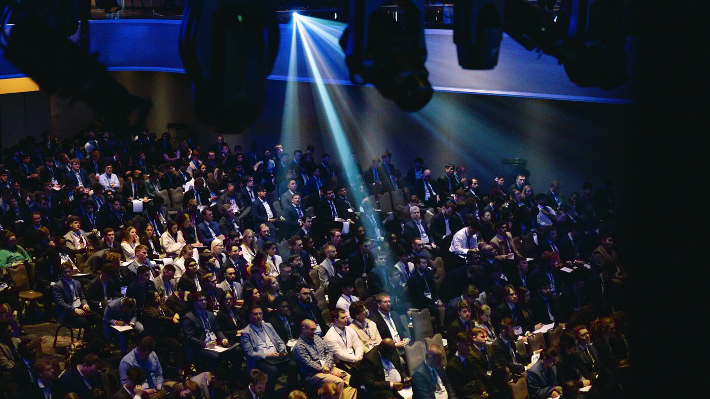 A spotlight shines down on a section of the seated audience in the middle of the forum.