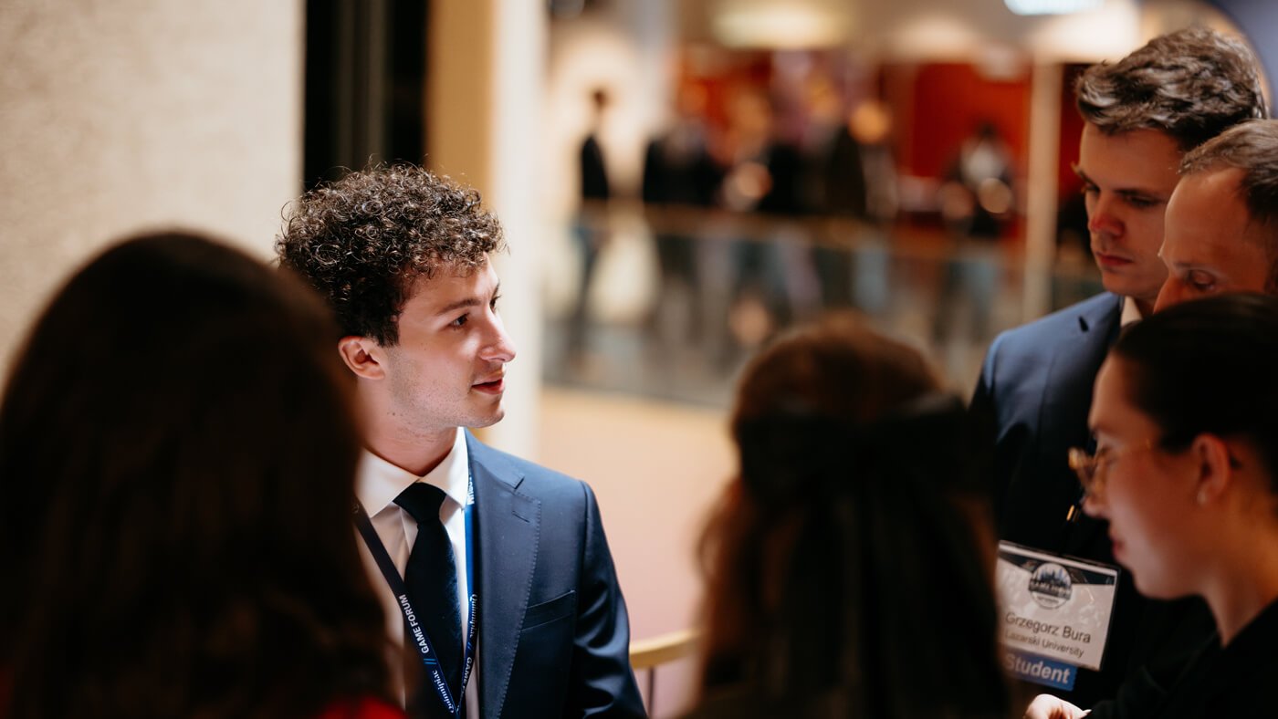 A student in a suit leads a discussion with peers during a breakout moment in the forum’s common area.