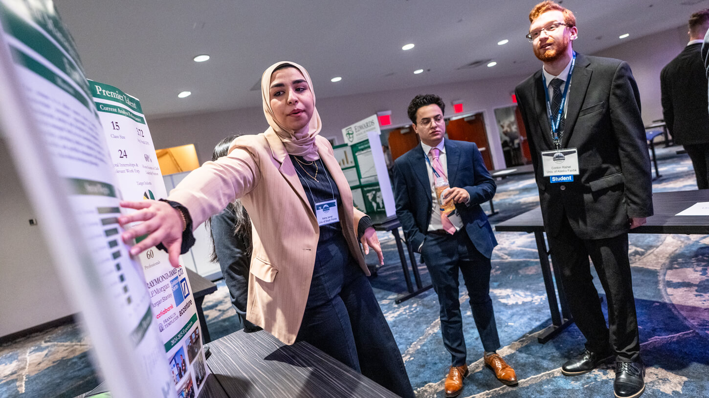 A student from the University of South Florida gestures toward her team’s green-and-white poster while explaining data points to fellow attendees at the GAME Forum.