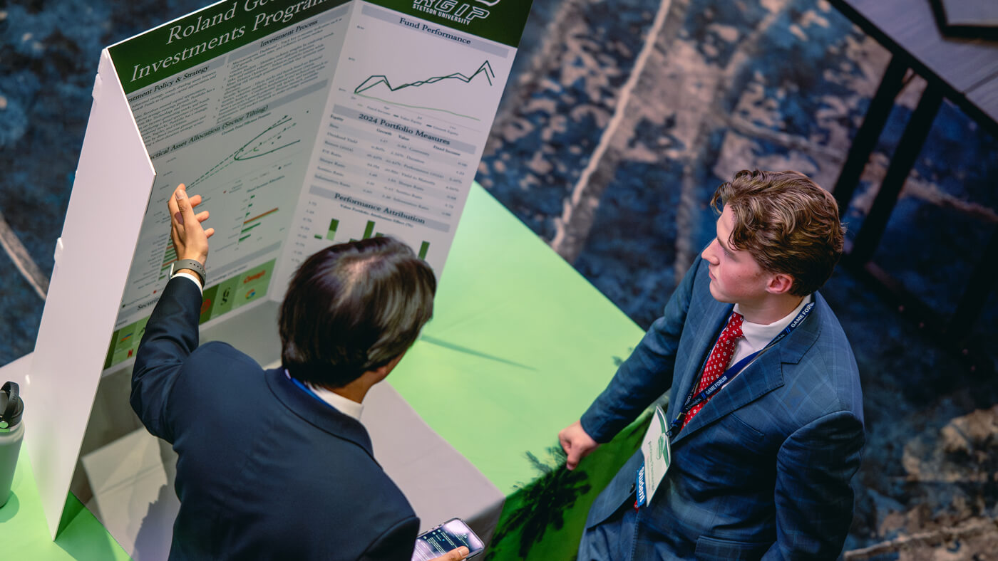 Two students from Stetson University stand beside a green-draped table and a financial portfolio poster with charts and fund performance metrics.