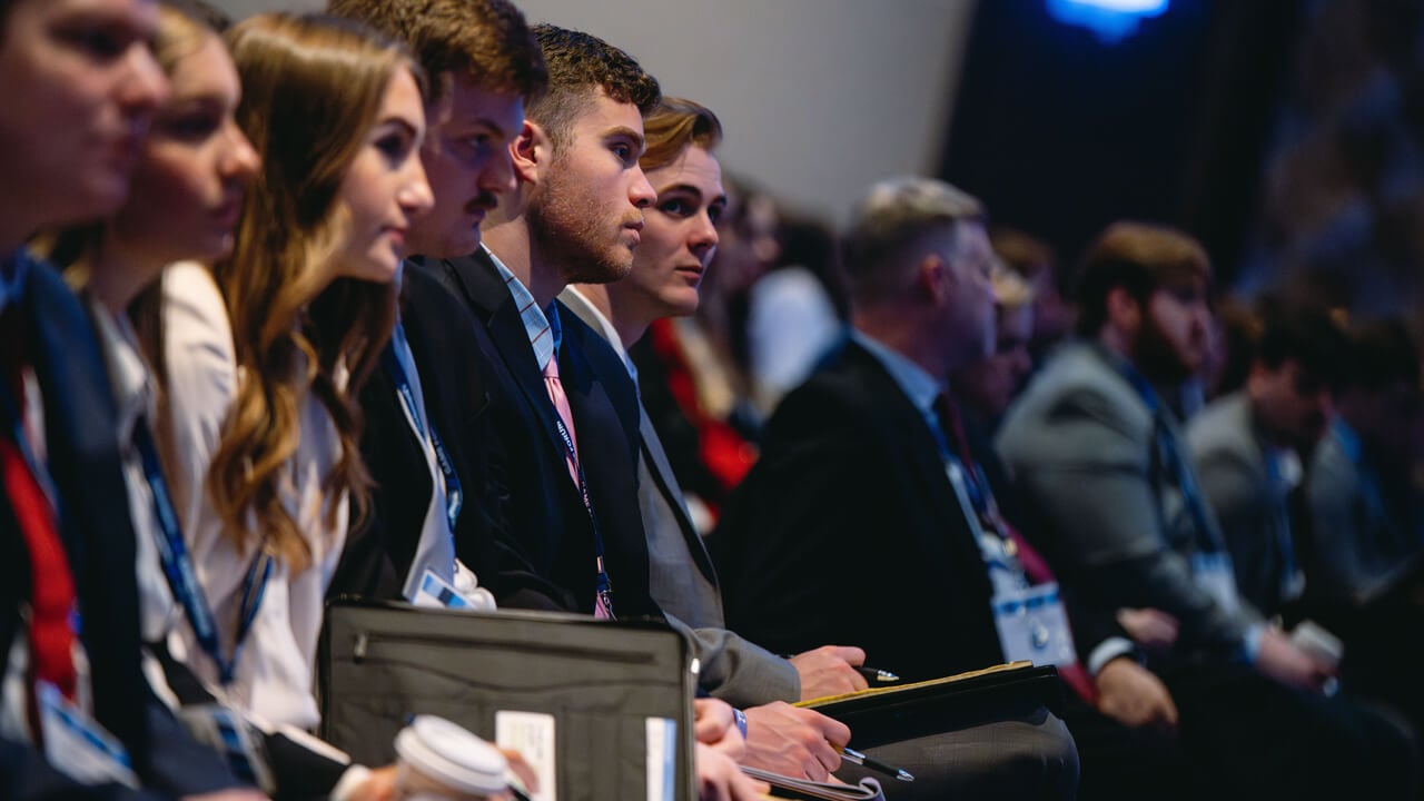 Students with pens and portfolios sit in the audience during GAME Forum